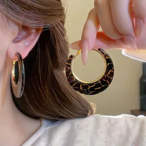 Close-up of large C-shaped flocking leopard hoop earrings with vintage gold crackle pattern