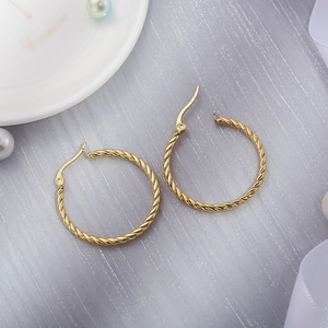 Detailed macro of gold twisted hoop earrings with a braided texture on silk fabric