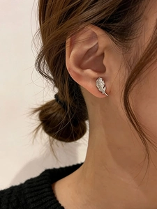 Macro shot of silver feather stud earring with sparkling cubic zirconia on model ear