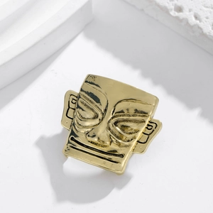 Close-up of polished gold face mask brooch with reflective metal texture on white background