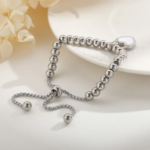 Détail du bracelet à billes argentées réglable avec breloque cœur blanc sur plateau