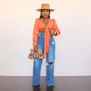 Detailansicht einer High-Waist-Jeans mit Rissen und einem orangefarbenen Crop-Top