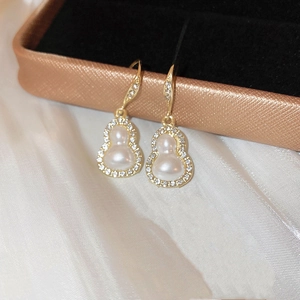 Detailed view of gold gourd earrings with pearls and diamonds on silk and jewelry box
