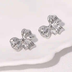 Elegant silver bow stud earrings in stainless steel on white ceramic plate