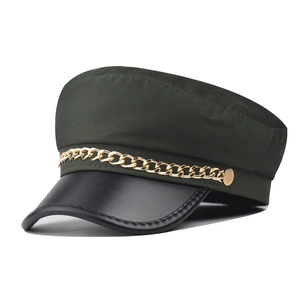 Close-up of baker boy hat with green twill fabric and gold chain detail on black brim