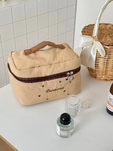 Détail d'une trousse à maquillage matelassée beige avec broderie et anses brunes