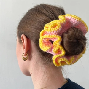 Detail of a large pink and yellow ruffled crochet hair scrunchie worn on a hair bun