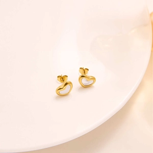 Close-up of golden heart earrings with white shell inlay on a ceramic display tray