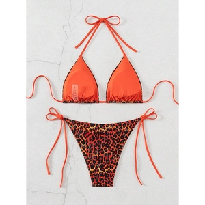 Flat lay of orange halter bikini top with leopard print side-tie bottoms on stone background