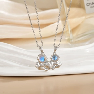 Close-up of astronaut couple necklace with blue zircon inlay on white silk backdrop