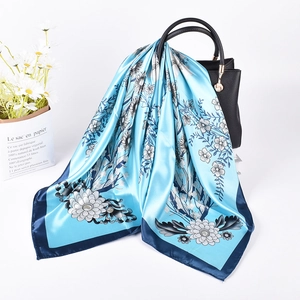 Detail of floral satin silk scarf with blue botanical prints draped over a leather bag
