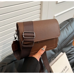 Detail of a brown leather crossbody bag with a wide canvas strap and metal buckle