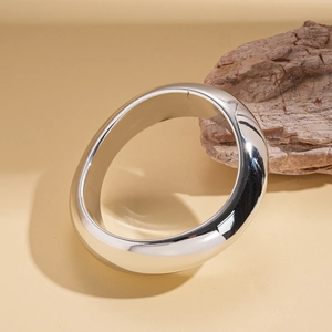 Macro shot of silver chunky open bangle with a polished mirror finish on beige surface