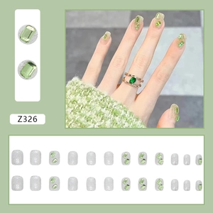 Detail of silver glitter press-on nails with green crystal rhinestones and matching gold ring