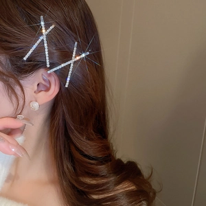 Close-up of sparkling X-shaped crystal hair clips on wavy brown hair with rhinestone detail