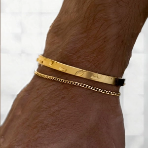 Close-up of men's layered gold Cuban chain bracelet and etched bangle with water droplets
