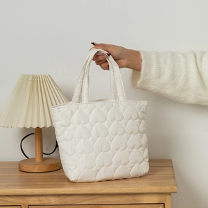 Detail of white heart-quilted fabric texture and sturdy handle on minimalist handbag