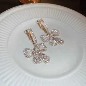 Close-up of golden bow earrings with white pearls and sparkling rhinestones on ceramic