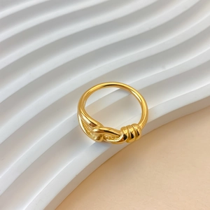 Dettaglio di un anello in acciaio inossidabile dorato con nodo su base ondulata.