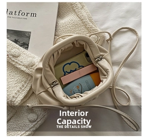 Interior storage space of a stylish cream dumpling bag showing phone and lipstick