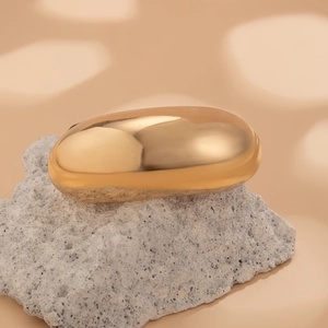 Detail of a minimalist gold oval metallic hair ring on a textured grey stone base