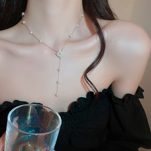 Collier élégant en perles avec pendentif fleur de camélia doré et gland porté par un mannequin