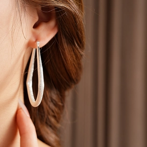 Gros plan de boucles d'oreilles créoles argentées mates portées par un modèle