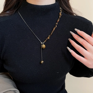 Detail of tiger eye beaded necklace with metal pendants on model wearing black sweater