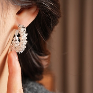 Detail of silver geometric hoop earring with layered woven texture on female ear