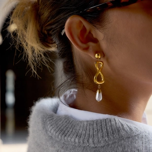 Boucles d'oreilles pendantes infini dorées avec perles blanches élégantes sur modèle