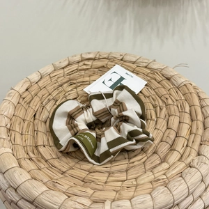 Striped knit scrunchie in green and brown tones with a brand tag on woven texture