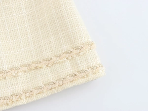 Gros plan détaillé sur le tissu tweed beige avec bordure tressée en fil doré et texture
