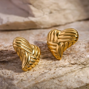 Detailed view of textured 18k gold heart stud earrings on a natural stone background