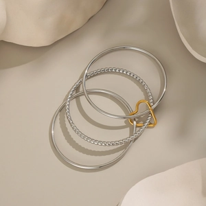 Multi-layer silver stainless steel rings set with a golden heart charm on beige background
