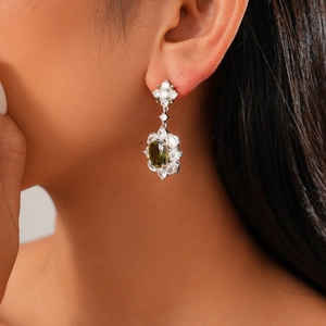 Close-up of model wearing silver flower earrings with green gemstone and zircon stones