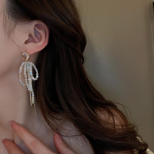Detail of elegant silver needle bow earrings featuring long white bead tassels and crystals