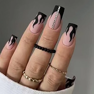 Long square press-on nails with nude pink base, black flame art, and silver rhinestones