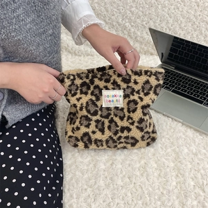 Detail of opening a plush leopard print cosmetic bag with soft texture on white carpet