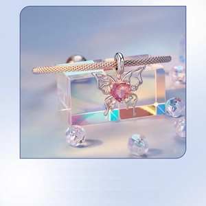 Detail of butterfly pendant with pink heart stone on rose gold braided bracelet