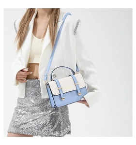 Detail of light blue and cream crossbody bag with gold metal lock and leather handle