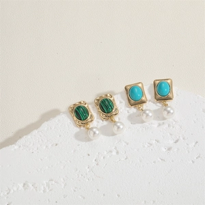 Emerald green stone and pearl earrings with gold frames on a textured white surface