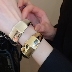 Detailed view of wave-textured metal open bangles in gold and silver finishes