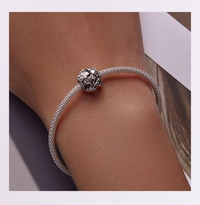 Close-up of bird and flower engraved silver bead charm on mesh bracelet for women