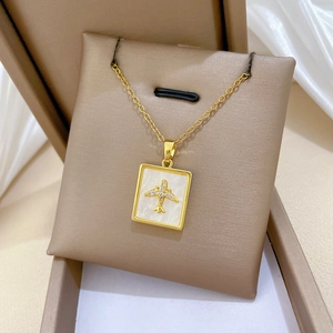 Detailed macro view of a gold airplane necklace with white shell pendant on a jewelry stand