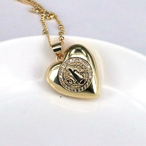 Close-up of golden heart pendant featuring St. Benedict medal and sparkling rhinestones