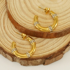 Gold stainless steel C-shape bamboo earrings with rhinestone accents on wood