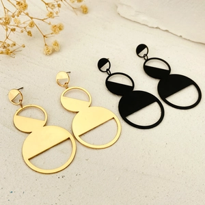 Exaggerated geometric round drop earrings in gold and matte black finish on stone background