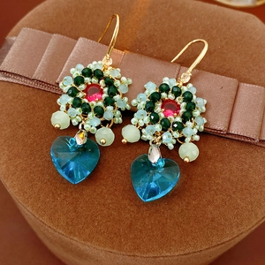 Dettaglio di orecchini vintage con perline a fiore e ciondolo a cuore in cristallo blu