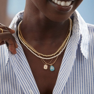 Layered gold necklaces with pearl strand, square letter S charm and blue teardrop pendant