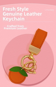 Detailed view of orange leather fruit keychain with gold hardware on pink surface